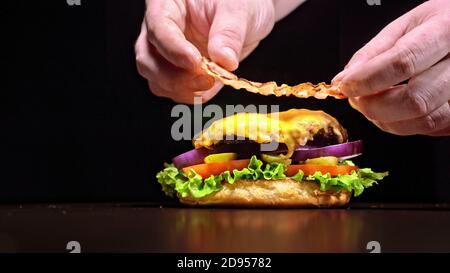 Handwerk Burger ist Kochen auf schwarzem Hintergrund. Bestehen: Sauce, Salat, Tomaten, Roten Zwiebeln, Gurke, Käse, Speck, Brötchen und marmoriertes Fleisch Rindfleisch. Stockfoto