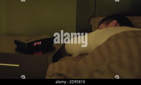 Ein Mann, der mit einem Wecker in seinem Bett schläft Weiter auf dem Nachttisch Stockfoto