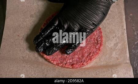 Kochen macht Fleisch Medaillons für Burger. Koch in schwarz Handschuhe macht Schnitzel essen. Die koteletts sind in Stahl Ring in eine noch Medaillon eingeebnet. Stockfoto