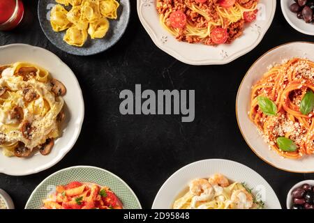 Italienische Pasta-Gerichte bilden einen Rahmen für Kopierraum, über Kopf auf einem dunklen Hintergrund aufgenommen. Pasta mit Fleisch, Gemüse, Meeresfrüchten, Huhn und Pilzen, mit Ravioli, Oliven Stockfoto