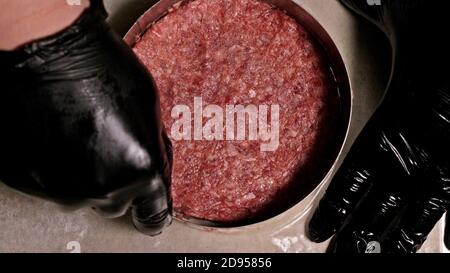 Kochen macht Fleisch Medaillons für Burger. Koch in schwarz Handschuhe macht Schnitzel essen. Die koteletts sind in Stahl Ring in eine noch Medaillon eingeebnet. Stockfoto