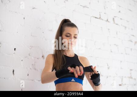 Ein Mädchen Boxer gegen eine weiße Ziegelwand wickelt ein Sportverband zum Boxen an den Händen Stockfoto