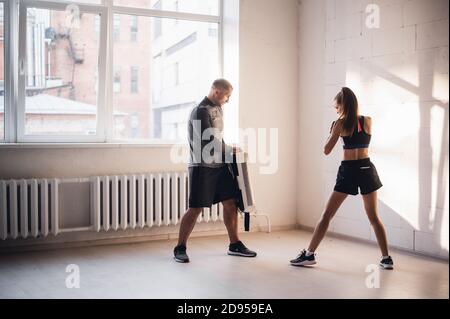 Trainingskampf von männlichen und weiblichen Kickboxern. Üben von Kicks und Schlägen auf der Boxpfote. Paarweise arbeiten Stockfoto