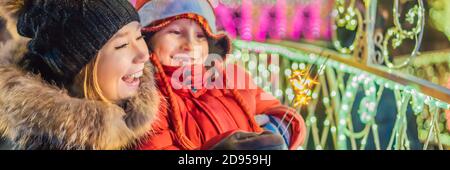 Kleiner Junge und seine Mutter mit Wunderkerzen in der Nähe von riesigen Tannenbaum und Weihnachtsbeleuchtung auf Weihnachtsmarkt. Weihnachten Feiertage auf fair. Crazy 2020 ist vorbei Stockfoto