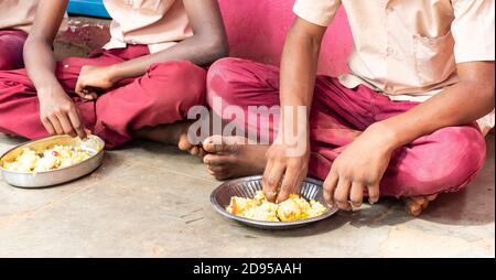 PUDUCHERRY, Tamil Nadu, Indien - Dezember Circa, 2018. Nicht identifizierte armen Mitschüler Kinder mit Uniformen sitzen auf dem Boden im Freien, Essen mit t Stockfoto