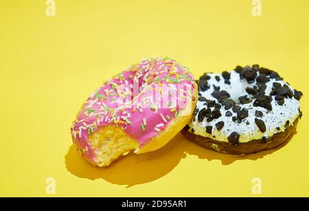 Rosa und weiße Donuts liegen auf einem gelben Hintergrund. Seitenansicht Stockfoto