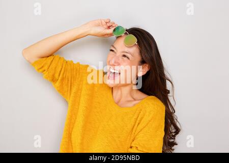 Nahaufnahme Porträt von stilvollen jungen asiatischen Frau lachen mit Sonnenbrille vor grauem Hintergrund Stockfoto