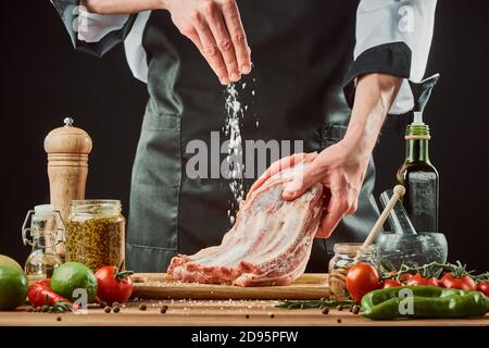 Der Koch salzt Roh-Rippchen und wirft eine große Prise auf das Stück Fleisch Stockfoto