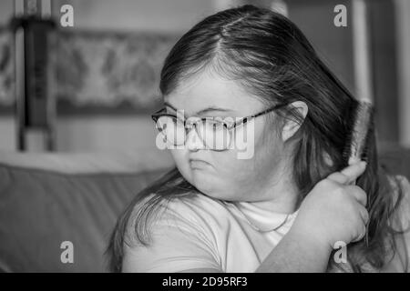 Junge Teenagerin mit Downs-Syndrom, die sich drinnen Haare putzt, Northampton, England, Großbritannien. Stockfoto