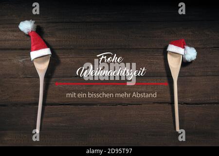 Zwei Kochlöffel mit roten Weihnachtsmannmützen, deutscher Text Frohe Weihnachtszeit mit ein bisschen mehr Stand, mean Merry Christmas with Social dist Stockfoto