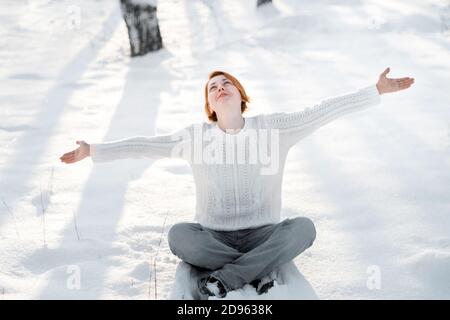 Ingwer Frau sitzt auf Schnee. Junge Frau im Winter Park. Freiheit und freudiges Konzept. Stockfoto
