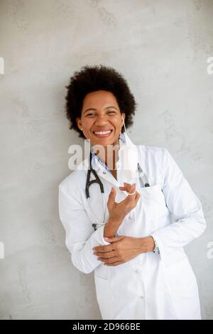 Weibliche afroamerikanische Arzt tragen weiße Uniform und Abheben Gesichtsmaske im Krankenhaus Stockfoto