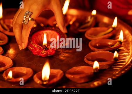 Happy Diwali Hintergrund. Nahaufnahme der weiblichen Hand, die eine beleuchtete Diya aus einem Puja thali nimmt. Konzept für indische traditionelle religiöse Puja Ritual festlich. Stockfoto