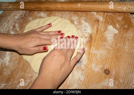 Frau Frau Hände Blick während der Vorbereitung hausgemachte Pizza mit Holz Nudelholz in der Küche, Lockdown Hausmannskost Stockfoto