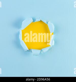 Geripptes Papierloch mit gelbem Hintergrund. Eingerissene Öffnung in blauem Papier, abgerissene Kanten. Platz für Ihr Design kopieren. Stockfoto