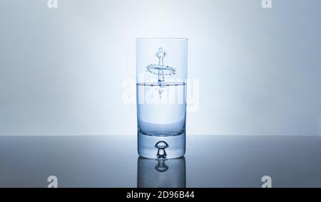 Abstrakt Wassertropfen Spritzer in Glas halb voll vor hellem Hintergrund. Stockfoto