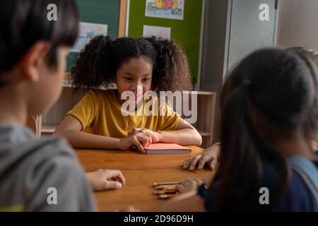 Ernsthafte afroamerikanische Schulmädchen Blick auf Kinder im Klassenzimmer, spielen ein Spiel, Herausforderung, Lernen, Zählen. Schulmädchen mit Händen auf dem Tisch konzentriert während der Herausforderung Stockfoto