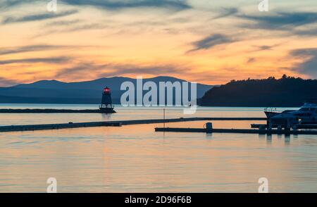 Sonnenuntergangsszene von Lake Champlain aus Burlington Vermont von einem Segelboot und Leuchtturm mit den Adirondack Mountains im Hintergrund. Stockfoto