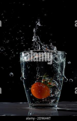 Eine saftige rote Tomate spritzt in ein Glas Wasser, Wasser spritzt herum Stockfoto