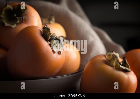 Stillleben mit Kakis und Kakimmon auf braunem Holztisch In Low-Key Stockfoto