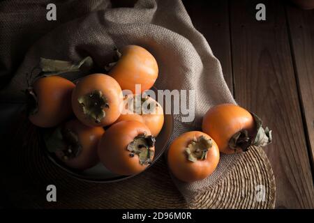 Stillleben mit Kakis und Kakimmon auf braunem Holztisch In Low-Key Stockfoto