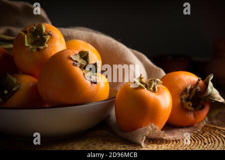 Stillleben mit Kakis und Kakimmon auf braunem Holztisch In Low-Key Stockfoto