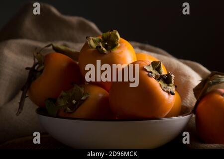 Stillleben mit Kakis und Kakimmon auf braunem Holztisch In Low-Key Stockfoto