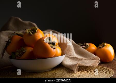 Stillleben mit Kakis und Kakimmon auf braunem Holztisch In Low-Key Stockfoto