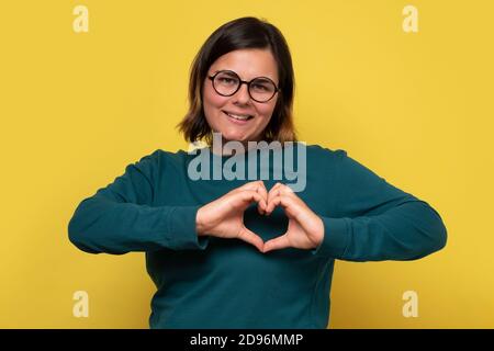 Junge Dame in Brille Blick auf die Kamera zeigt Herz Liebe Geste. Stockfoto