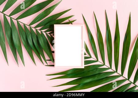 Elegante, minimalistische Komposition mit Fotorahmen und grünen Blättern auf einem rosa, pastellfarbenen Hintergrund. Bildvorlagen-Mockup mit Kopierbereich Stockfoto