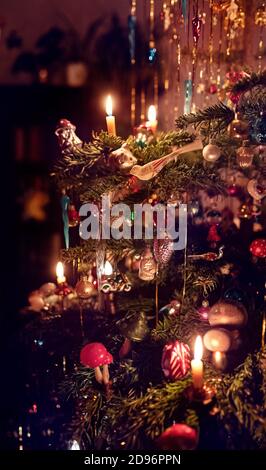 Ein Detail eines klassischen deutschen Weihnachtsbaums mit echten Kerzen und viel Lametta. Beleuchtet durch Kerzenlicht mit vielen verschiedenen Ornamenten. Stockfoto