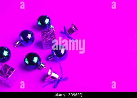 Weihnachtskugeln, Geschenke und funkelnde Glocken in Neonlicht auf rosa Hintergrund. Stockfoto