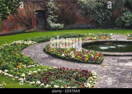 Schöner englischer Landgarten mit Blumenbeeten, einer umgebenden Mauer und Steinweg mit Brunnen Stockfoto