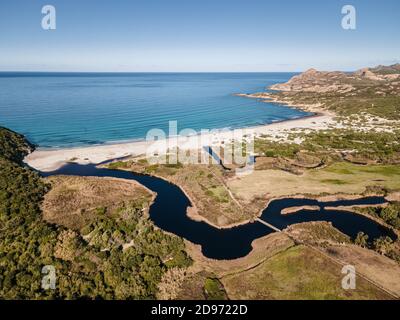 Luftaufnahme des türkisfarbenen mittelmeers, das auf das Meer wascht Weißer Sandstrand von Ostriconi in der Region Balagne Korsika mit einem Fluss schlängelt sich ich Stockfoto