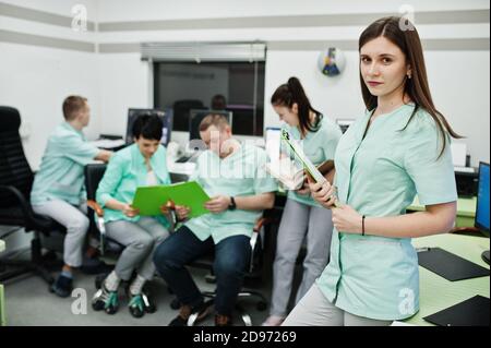 Medizinisches Thema .Porträt der weiblichen Ärztin mit Zwischenablage gegen Gruppe von Ärzten Treffen in der mrt-Büro im diagnostischen Zentrum im Krankenhaus. Stockfoto