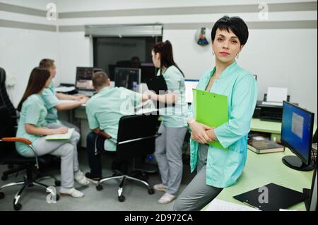Medizinisches Thema .Porträt der weiblichen Ärztin mit Zwischenablage gegen Gruppe von Ärzten Treffen in der mrt-Büro im diagnostischen Zentrum im Krankenhaus. Stockfoto