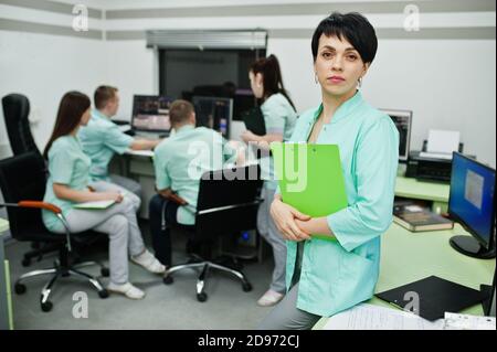 Medizinisches Thema .Porträt der weiblichen Ärztin mit Zwischenablage gegen Gruppe von Ärzten Treffen in der mrt-Büro im diagnostischen Zentrum im Krankenhaus. Stockfoto