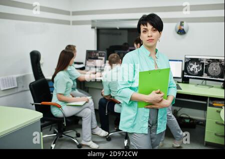 Medizinisches Thema .Porträt der weiblichen Ärztin mit Zwischenablage gegen Gruppe von Ärzten Treffen in der mrt-Büro im diagnostischen Zentrum im Krankenhaus. Stockfoto