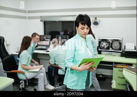 Medizinisches Thema .Porträt der weiblichen Ärztin mit Zwischenablage gegen Gruppe von Ärzten Treffen in der mrt-Büro im diagnostischen Zentrum im Krankenhaus. Stockfoto