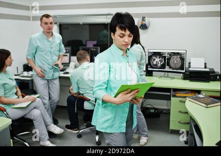 Medizinisches Thema .Porträt der weiblichen Ärztin mit Zwischenablage gegen Gruppe von Ärzten Treffen in der mrt-Büro im diagnostischen Zentrum im Krankenhaus. Stockfoto