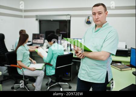 Medizinisches Thema .Porträt des männlichen Arztes mit Zwischenablage gegen Gruppe von Ärzten Treffen in der mrt-Büro im diagnostischen Zentrum im Krankenhaus. Stockfoto