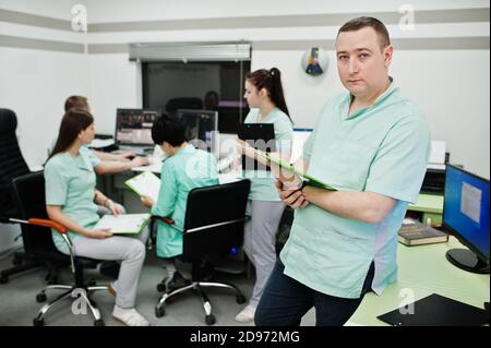 Medizinisches Thema .Porträt des männlichen Arztes mit Zwischenablage gegen Gruppe von Ärzten Treffen in der mrt-Büro im diagnostischen Zentrum im Krankenhaus. Stockfoto