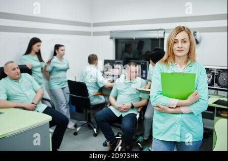 Medizinisches Thema .Porträt der weiblichen Ärztin mit Zwischenablage gegen Gruppe von Ärzten Treffen in der mrt-Büro im diagnostischen Zentrum im Krankenhaus. Stockfoto