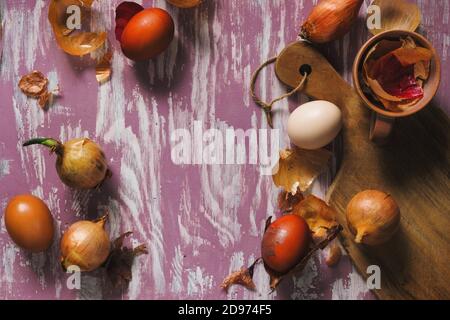 Eier und Zwiebeln auf einem rustikalen Tisch, Blick von oben. Ostereier in traditionellen natürlichen Farbstoff gefärbt - Zwiebelhäute. Polnische Ostertradition. Stockfoto