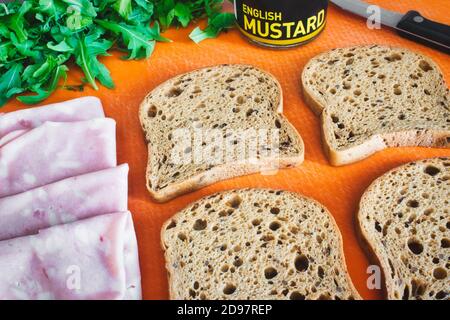 Scheiben Vollkornbrot auf einem Schneidebrett mit Schinken, Rucola und englischem Senf ausgelegt Stockfoto