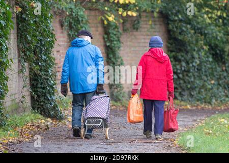 Rückansicht eines Rentnerpaares, das mit Einkaufstaschen und Einkaufskorubus nach Hause geht, bevor England in die zweite Coronavirus-Sperre geht. Stockfoto