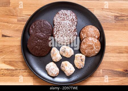 Deutsche runde Lebkuchen und deutsche Stollenstücke auf schwarzem Teller. Holzhintergrund. Weihnachtliche Wüste, Snack. Stockfoto