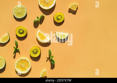 In Scheiben geschnittene Früchte Kiwi, Zitrus- und Minzblätter auf orangefarbenem Hintergrund Stockfoto