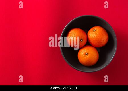 Frische Mandarinen in schwarzer Schale auf rotem Hintergrund Stockfoto
