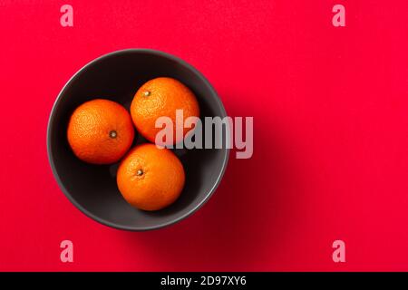 Frische Mandarinen in schwarzer Schale auf rotem Hintergrund Stockfoto